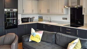 Une cuisine moderne avec des meubles de couleur sombre, un canapé gris, une chaise rouge et un four à micro-ondes.