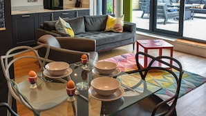 Une cuisine moderne avec des meubles de couleur sombre, une table à manger en verre avec des chaises, et un canapé gris agrémenté de coussins.