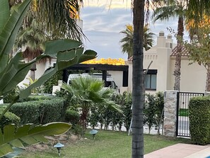 Un edificio moderno con techo plano, rodeado de vegetación cuidada y un muro de piedra.