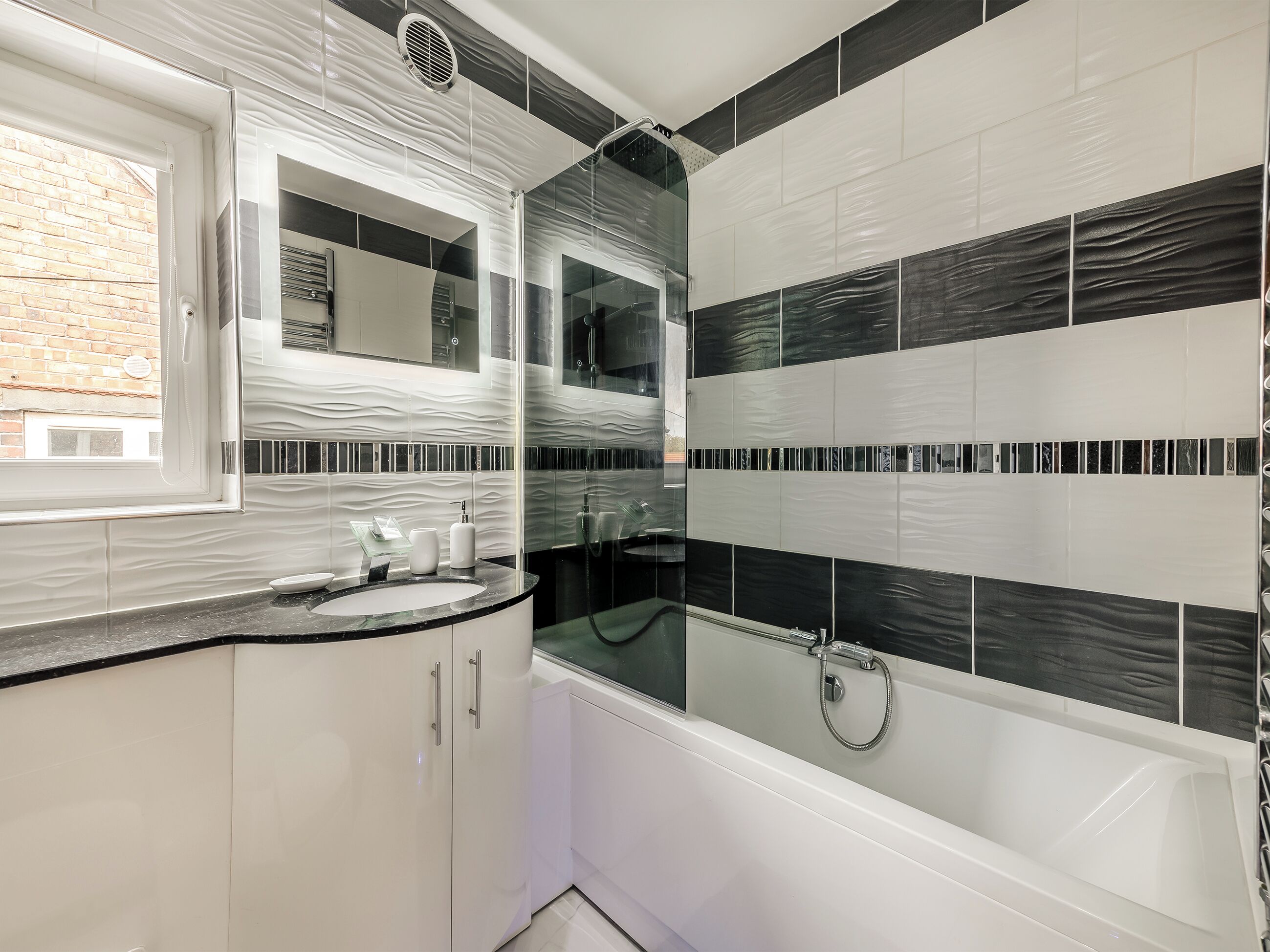 Un bany modern amb plat de dutxa de vidre, una banyera blanca i un lavabo amb rentapès i mirall.