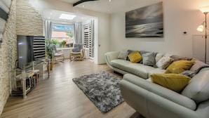 A modern living room with a sofa, a TV, a bookshelf, and a view of the outdoors.