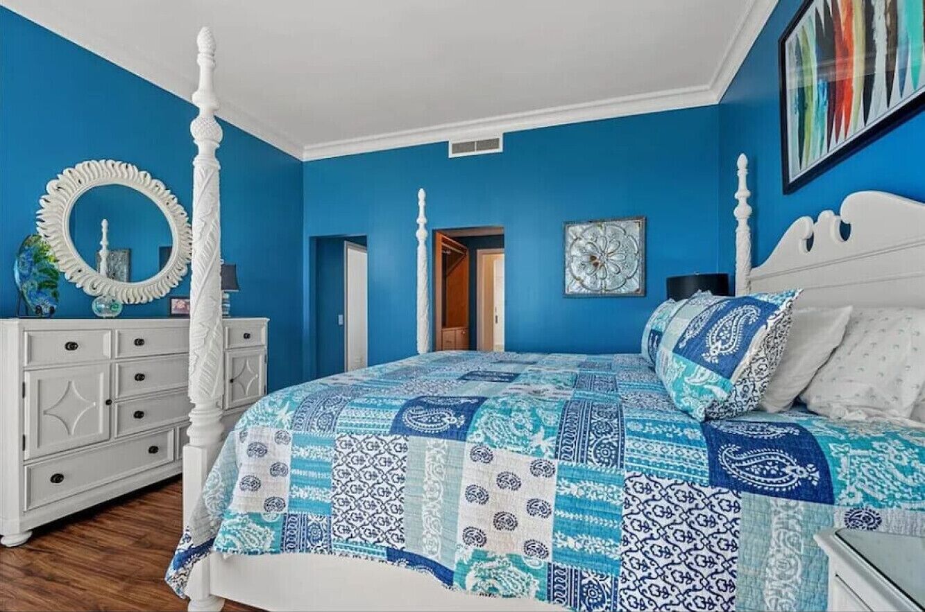 Un dormitorio con cama con dosel, un tocador blanco, un espejo redondo y una pared azul.