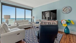 A living room with a large window, a sofa, a chair, a TV, and a decorative vase. - Ocean Creek Penthouse North Myrtle Beach (Myrtle Beach)