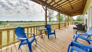 A covered outdoor deck with blue Adirondack chairs, a small round table, and a grill area. - Pet-Friendly Eagletown Home ~ 3 Mi to Kayaking! (Eagletown)
