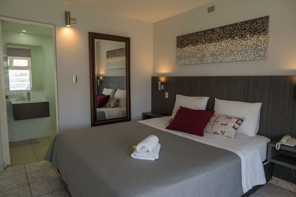 Une chambre d’hôtel avec un grand lit, une table de chevet avec un téléphone, un miroir et une œuvre d’art accrochée au mur.