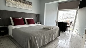 Habitación de hotel moderna con una cama grande, televisión de pantalla plana, una mesa de comedor y un balcón con vistas a la ciudad.