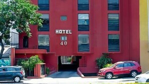 Un edificio de hotel rojo con el número 40 en la fachada, múltiples ventanas y una pequeña zona de entrada con un coche estacionado cerca.
