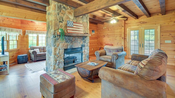 A log cabin interior with a stone fireplace, wooden furniture, and a stone pillar with an American flag. - Peaceful Raphine Cottage w/ Deck & Fireplace! (Raphine)
