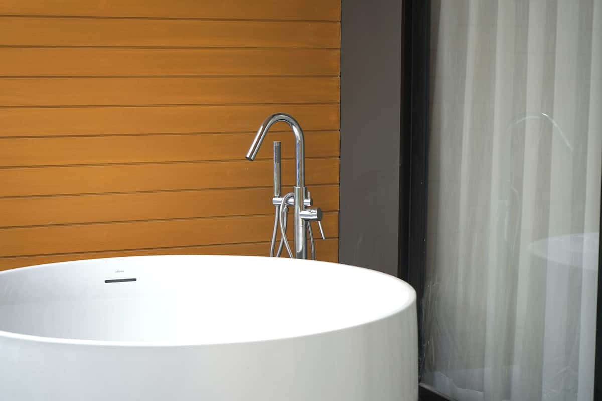 Un baño moderno con una bañera blanca grande, un grifo de cromo y paneles de madera en la pared.