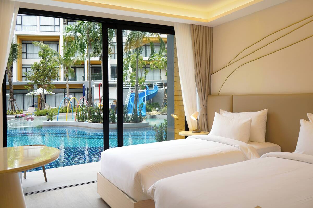 Habitación de hotel con una cama grande, una mesita pequeña y vistas a una piscina y un tobogán.