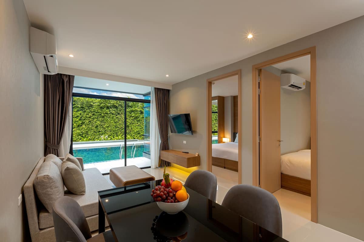 Una habitación de hotel moderna con un sofá, una mesa de comedor con frutero, un televisor y una cama.