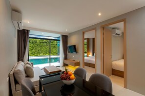 Una habitación de hotel moderna con un sofá, una mesa de comedor con frutero, un televisor y una cama.