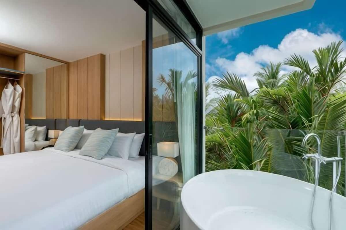 Un dormitorio moderno con una cama grande, un baño con paredes de vidrio y vistas a palmeras.
