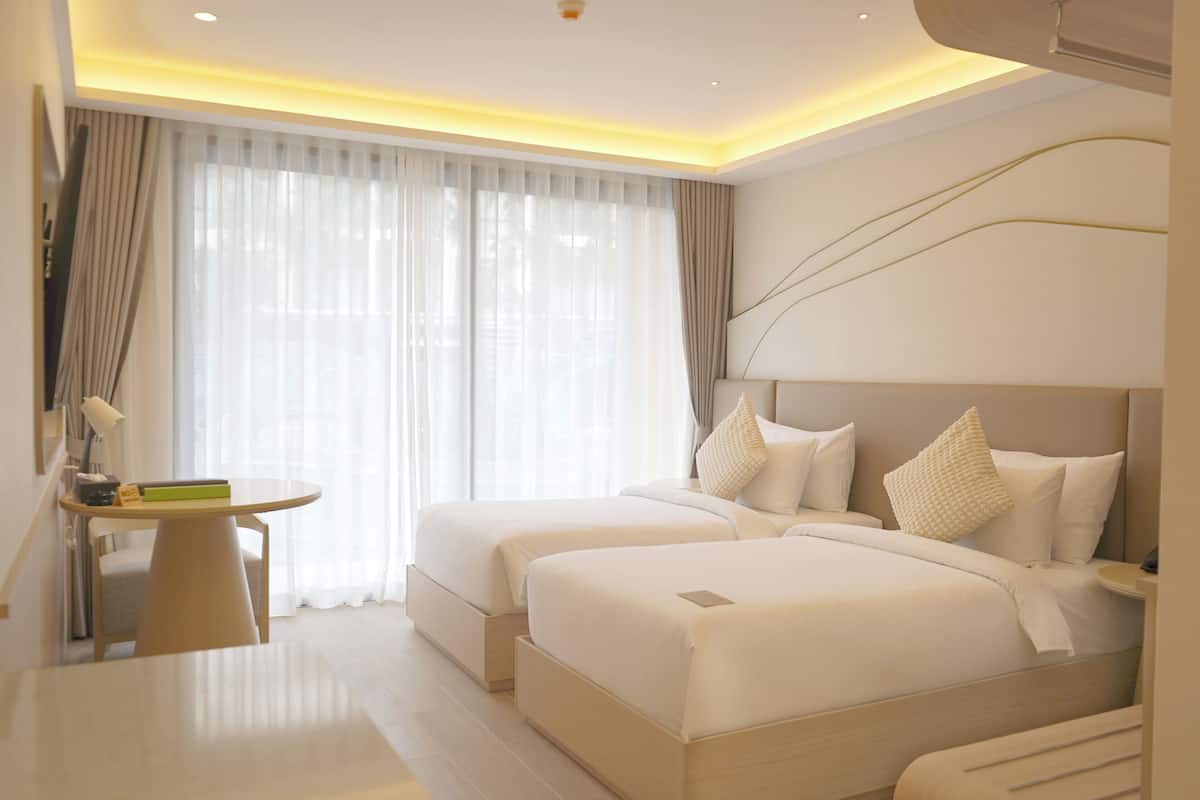 Una habitación de hotel con dos camas, un escritorio y un amplio ventanal con cortinas.