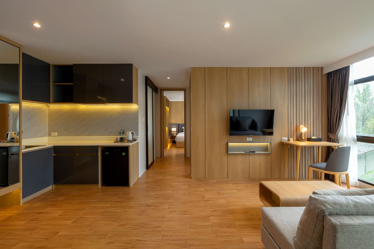 Habitación de hotel moderna con cocina, zona de estar con televisor y vistas al exterior.