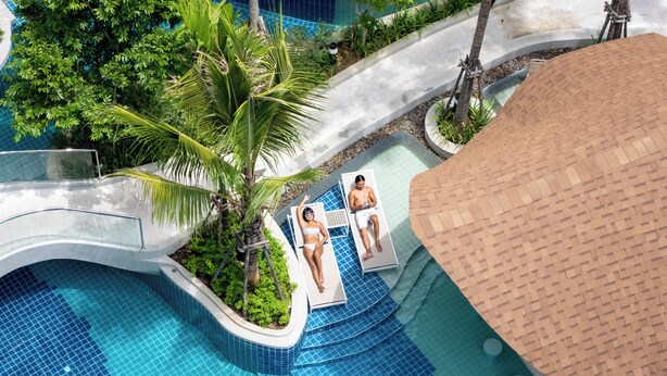 Un espace piscine doté d’un mur incurvé en verre, de palmiers et de chaises longues.