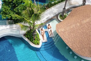 Un espace piscine doté d’un mur incurvé en verre, de palmiers et de chaises longues.