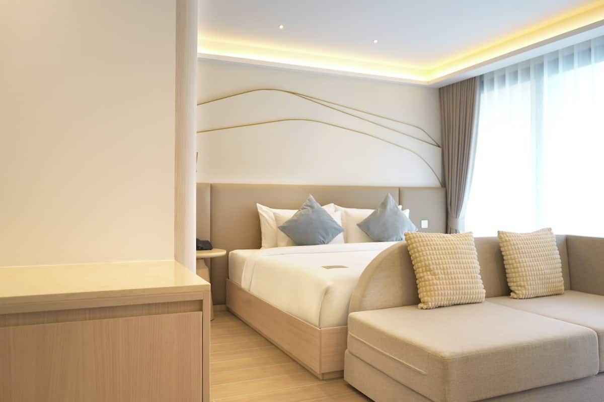 Una habitación de hotel moderna con cama, sofá, mesita de noche y escritorio.