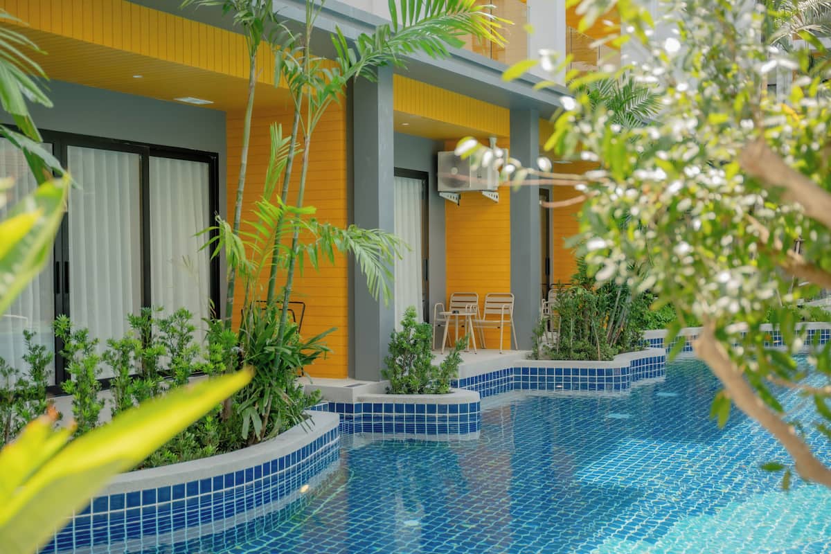 Piscina interior moderna con bordes de azulejos azules, rodeada de exuberante follaje y una terraza de madera con sillas.