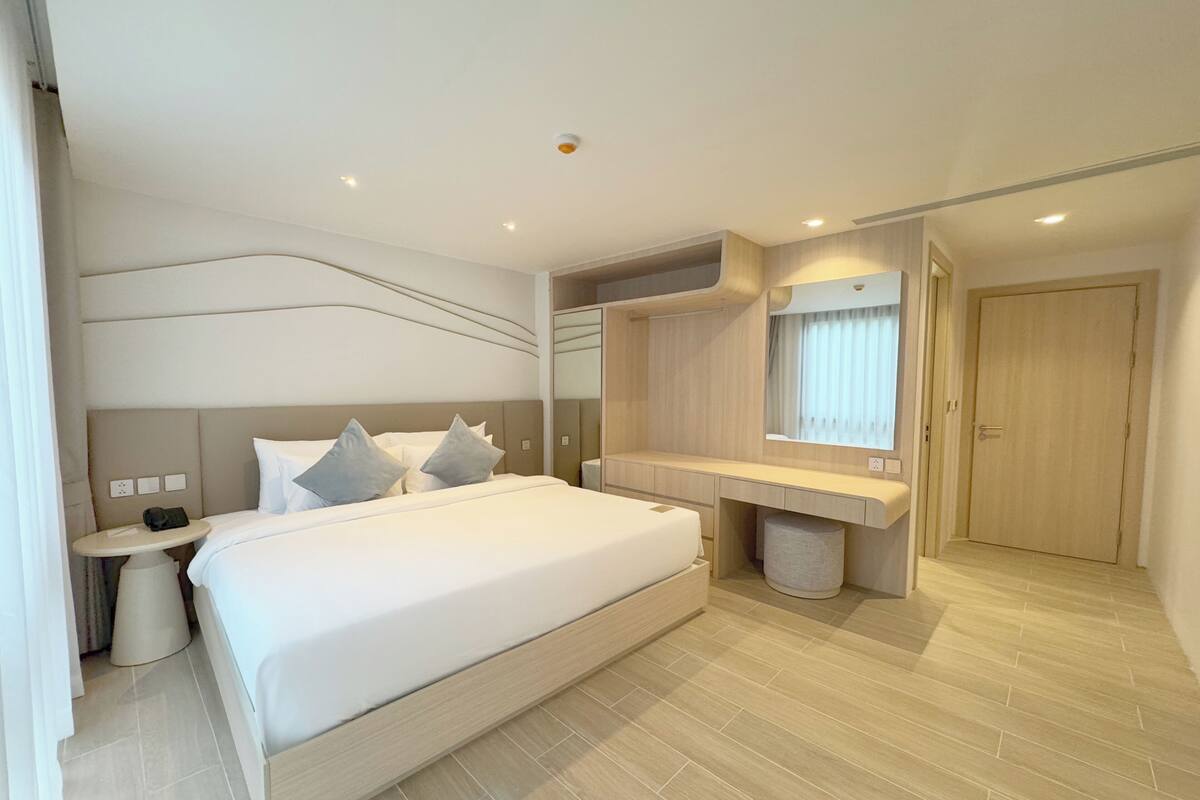 Una habitación de hotel moderna con una cama grande, una mesita de noche y un espejo sobre el tocador.