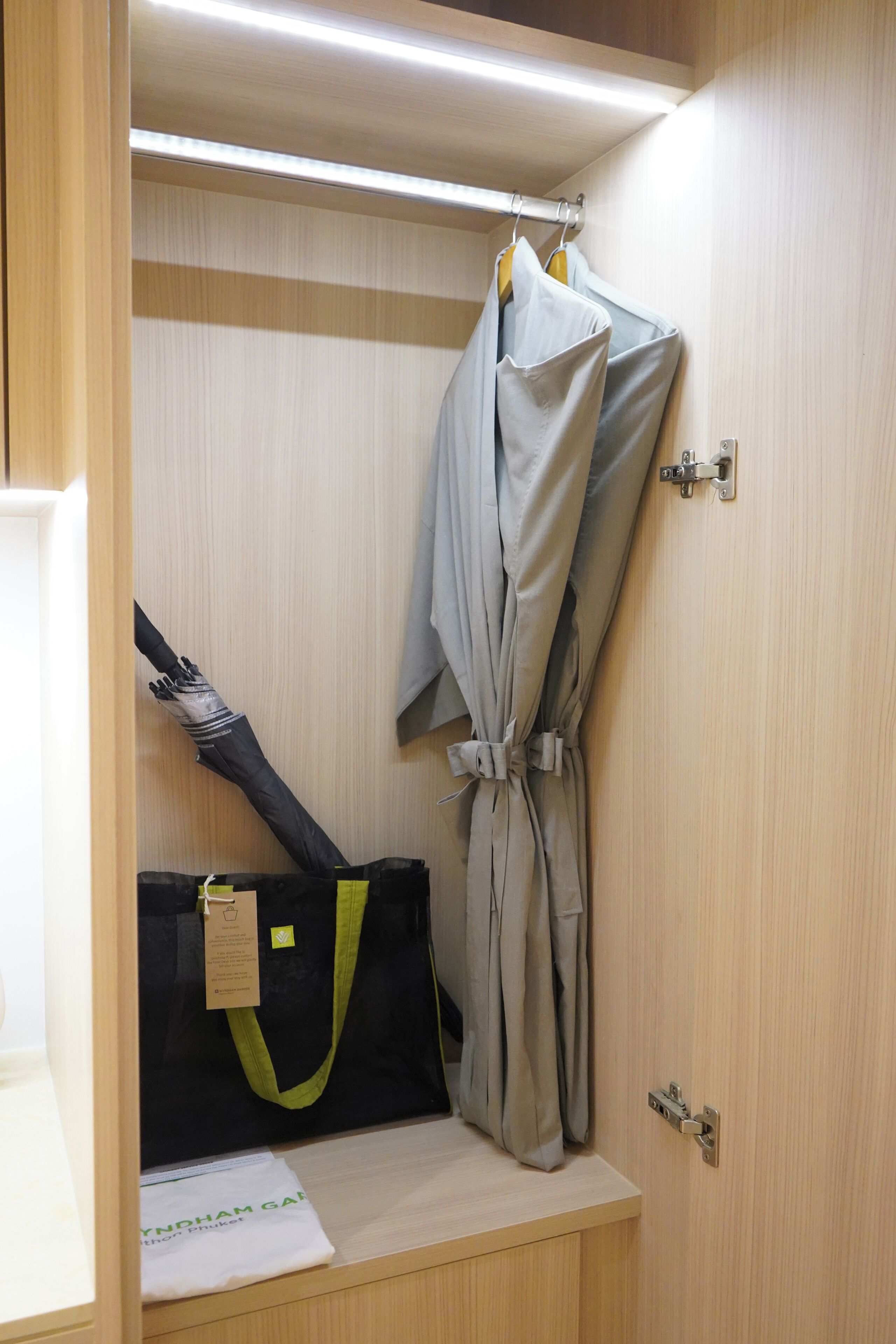 A compact room with a wooden wardrobe, a hanging rack, and a small table with a bag and a tag.
