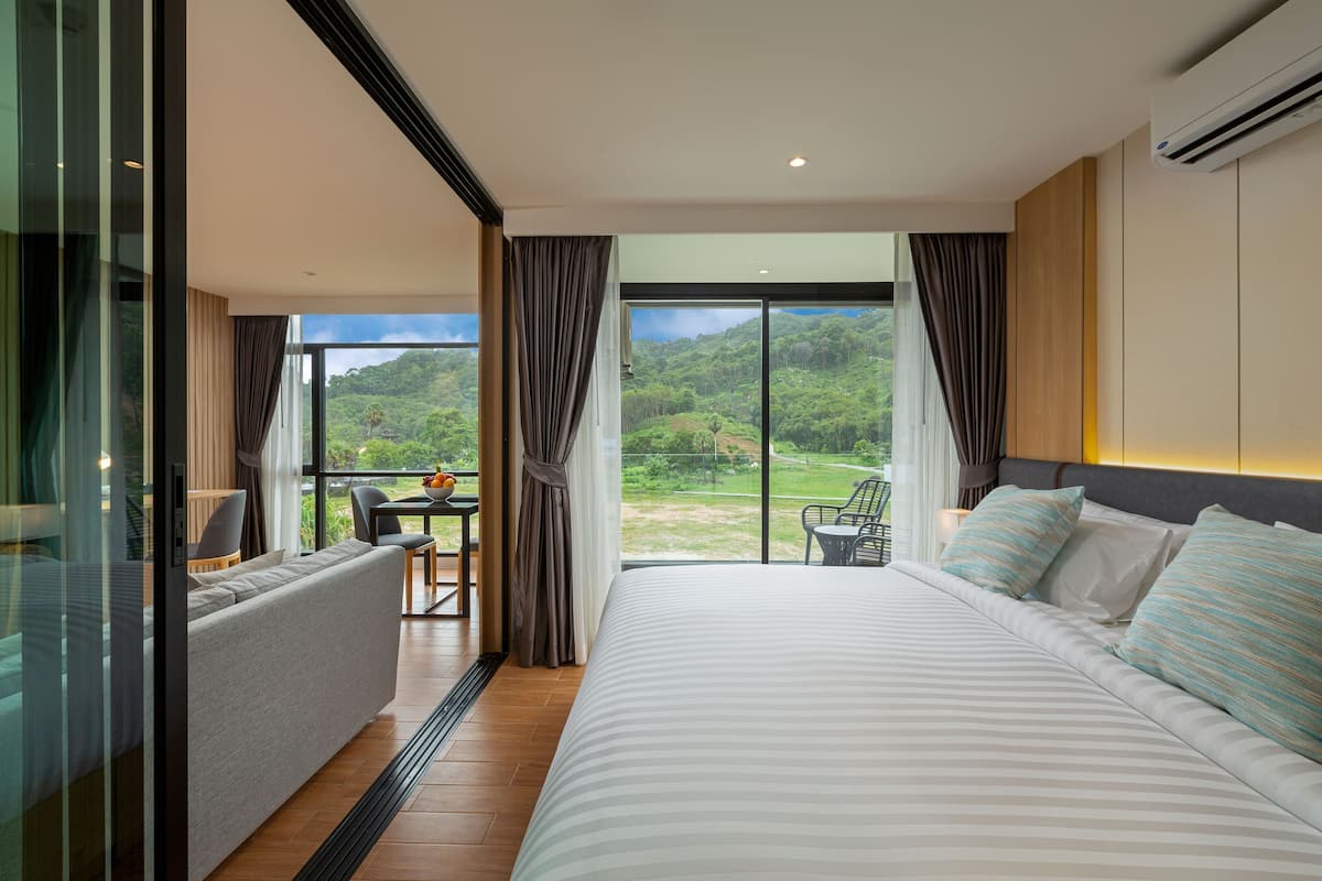 Una habitación de hotel moderna con una cama grande, un sofá, un comedor y vistas a un paisaje exuberante.