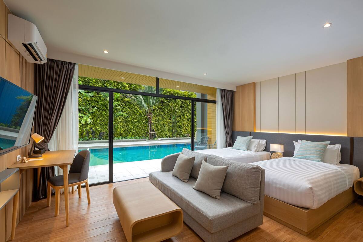Una habitación de hotel moderna con un ventanal grande, vistas a una piscina, un escritorio con lámpara, dos camas y un sofá.