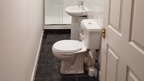 A narrow bathroom with a toilet, sink, and glass-enclosed shower. - Cosy pub flat in Shotts between Glasgow and Edinburgh (Shotts)