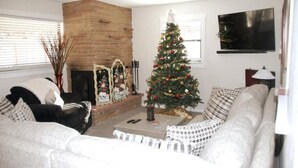 Una sala de estar con chimenea de ladrillo, un árbol de Navidad, un sofá y un televisor.