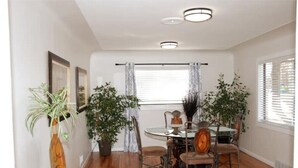 Un comedor con una mesa redonda, sillas, plantas en macetas y cuadros en la pared.