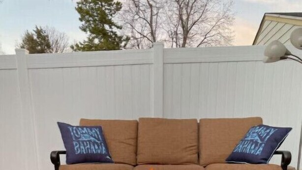 Un hogar cuadrado de metal con llamas frente a un sofá marrón con dos almohadas azules.