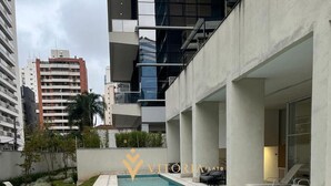 A swimming pool with lounge chairs, surrounded by a concrete deck and a grassy area. - Elegance Suítes Carvalho (São Paulo)