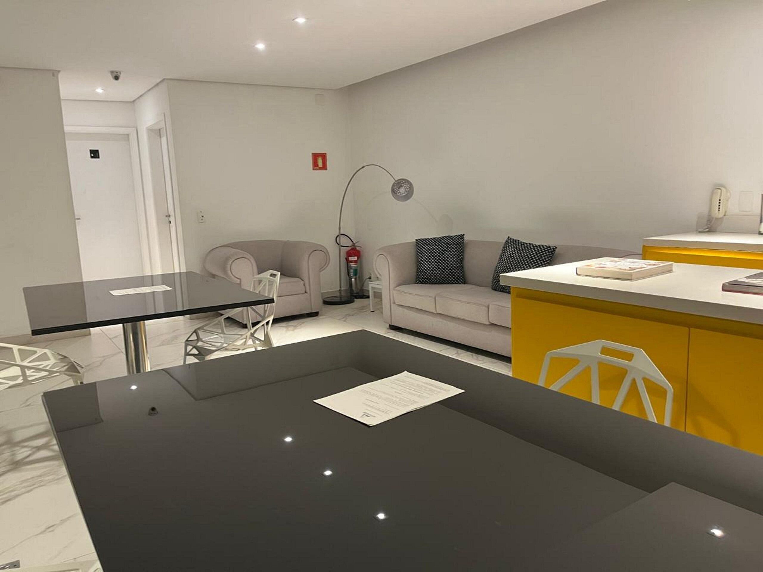 A modern, well-lit room with a glass dining table, a sofa, and a yellow counter.