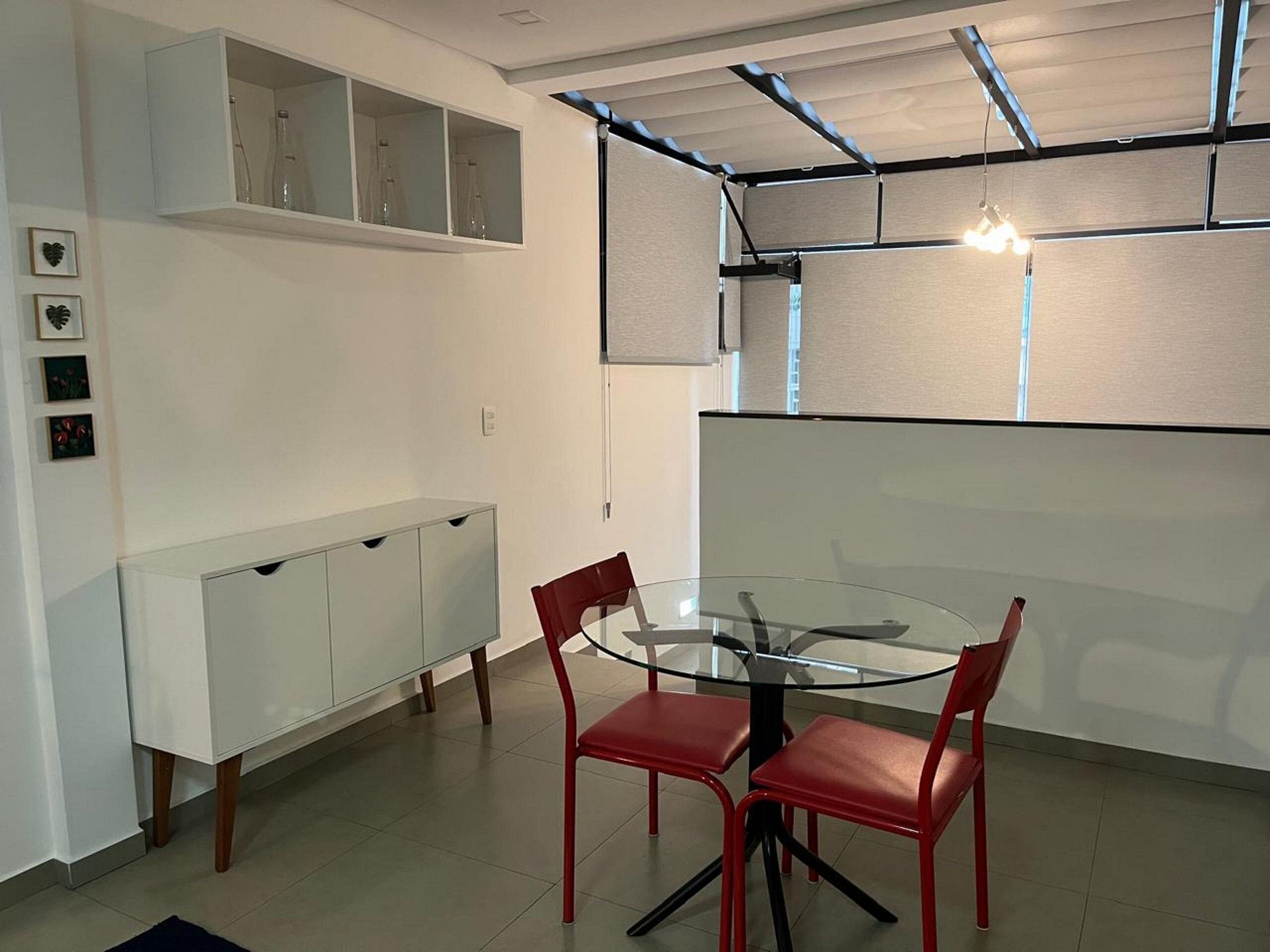 A modern dining area with a glass table and red chairs, white cabinets, and a ceiling with exposed beams and lighting.