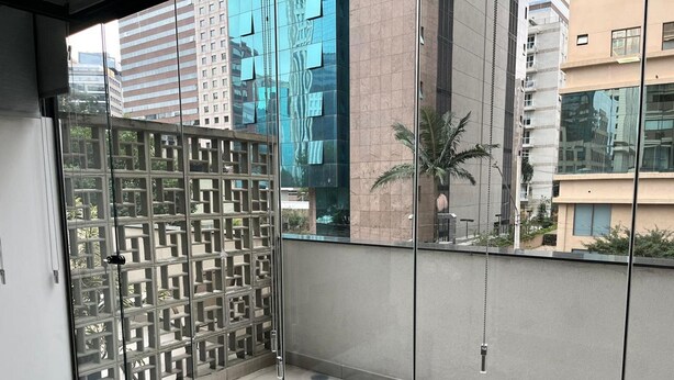 A modern balcony with a grey sofa, a decorative metal partition, and a view of surrounding buildings. - Elegance Suítes Carvalho (São Paulo)