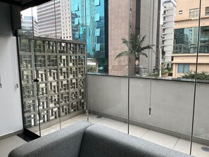 A modern balcony with a grey sofa, a decorative metal partition, and a view of surrounding buildings. - Elegance Suítes Carvalho (São Paulo)