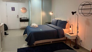 A modern bedroom with a bed, bedside tables, a desk, a chair, a floor lamp, and a wardrobe. - Elegance Suítes Carvalho (São Paulo)