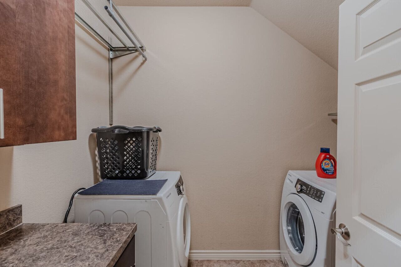 A laundry room with two washing machines, a drying rack, and a bottle of detergent.