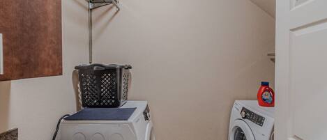 A laundry room with two washing machines, a drying rack, and a bottle of detergent.