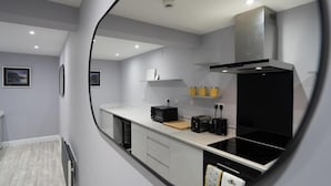 A modern kitchen with white cabinets, a black stove, and a microwave. There are two yellow containers on a shelf above the stove. - Indigo Apartment - Beautiful 1-bed in Ballycastle (Ballycastle)