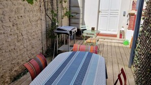 En overdækket terrasse med et bord og stole, en murstensvæg og en garageport i baggrunden.