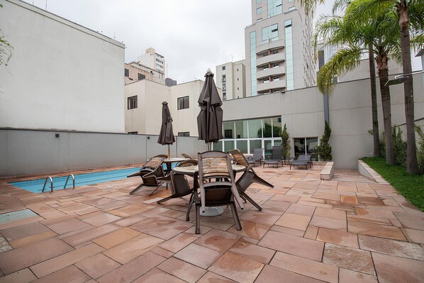 A rooftop pool area with lounge chairs and umbrellas, surrounded by buildings.