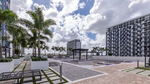 Un'area esterna moderna con zona salotto, palme e vista su un grattacielo.