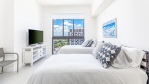 Camera da letto con un letto, una TV su un mobile bianco, una sedia e un'ampia finestra con vista sulla città.