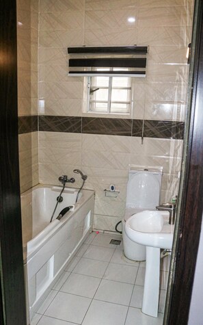 Bathroom features a bathtub, toilet, and window above the toilet, with a shelf for storage.