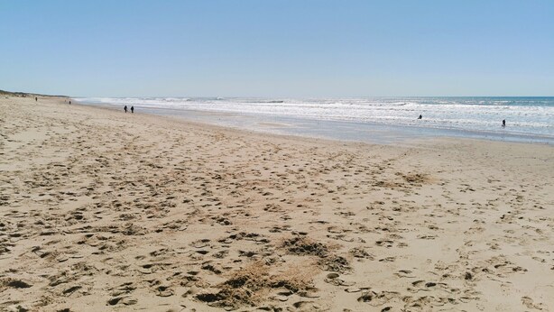 Ein breiter, sandiger Strand mit Fußspuren und einigen Spaziergängern.
