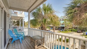 A wooden deck with blue Adirondack chairs and a glass table, overlooking a swimming pool and a parking area with cars and palm trees.