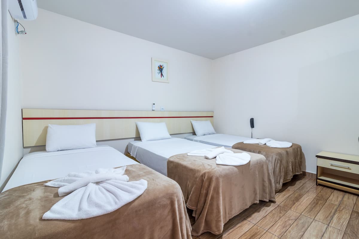 Ein Hotelzimmer mit drei Betten, jeweils mit brauner Bettdecke und weißen Handtüchern. Ein Nachttisch mit Telefon und einer kleinen Ablagefläche.