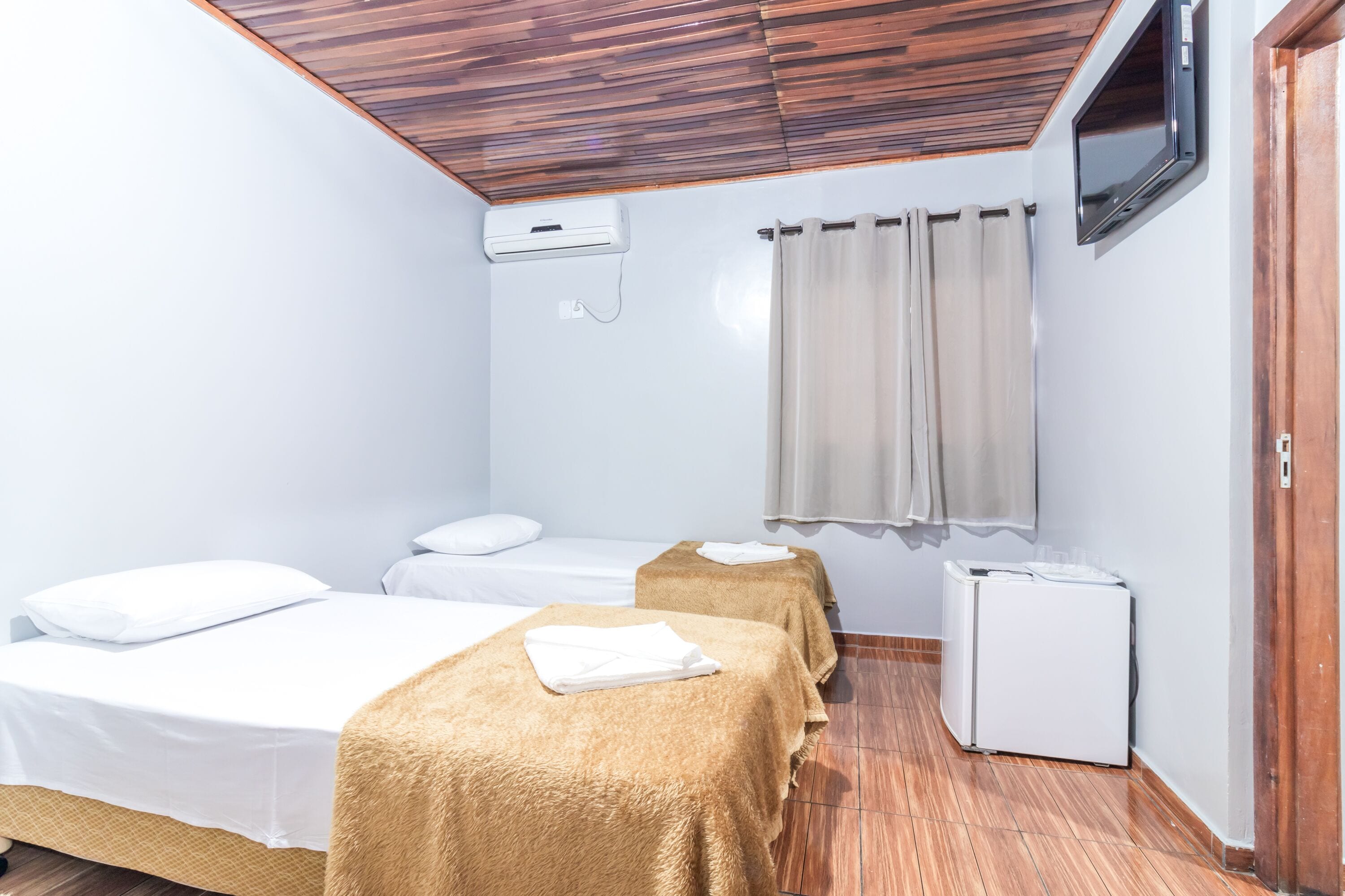 Une chambre avec deux lits, un petit réfrigérateur, une télévision et un plafond en bois.