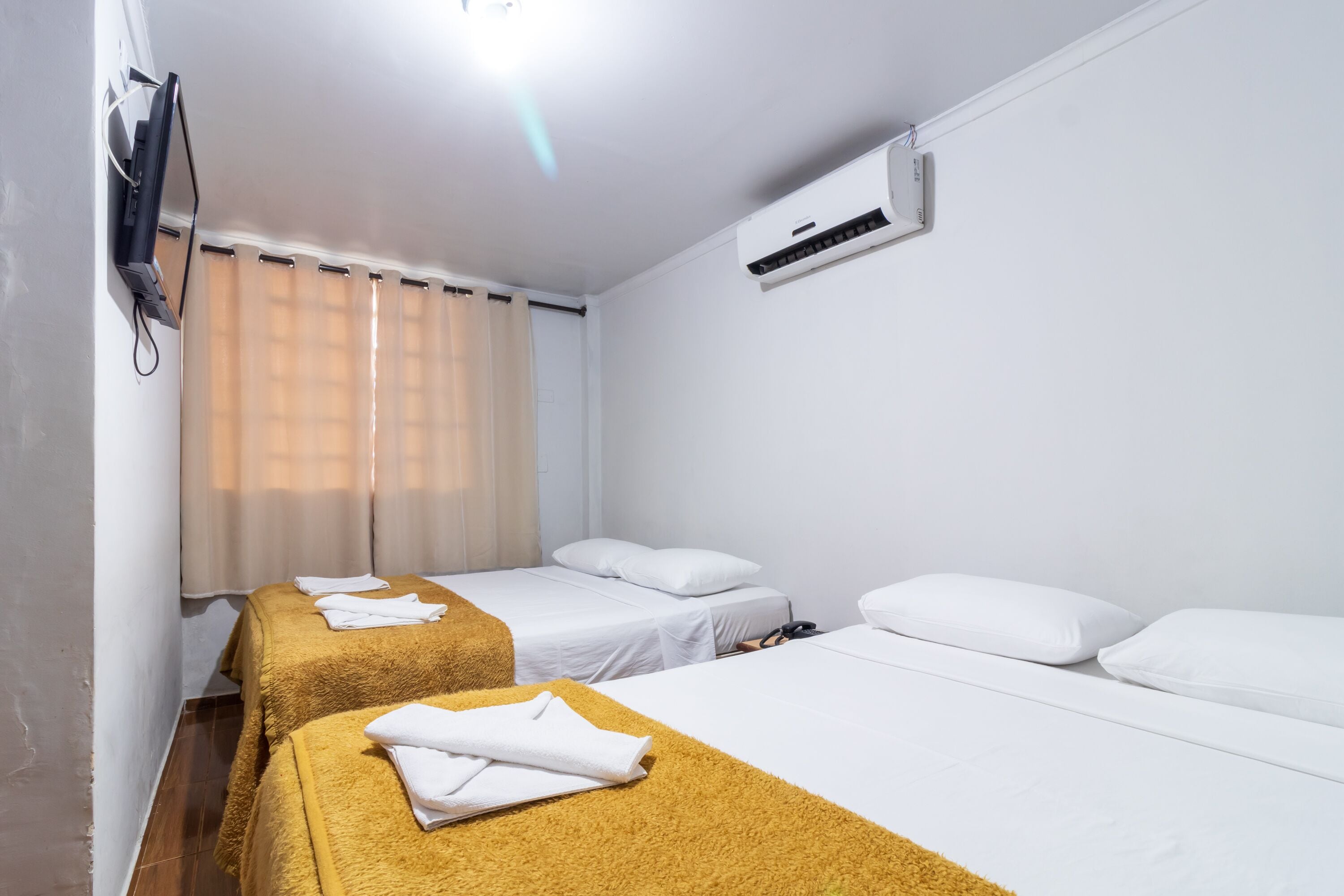 Hotellihuone, jossa on kaksi erillistä sänkyä, seinälle asennettu taulutelevisio ja ilmastointilaite.